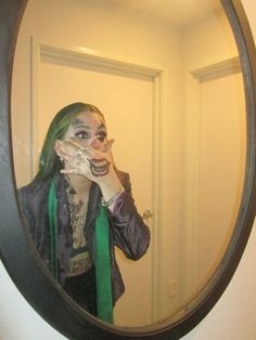 a woman with green hair and makeup in front of a mirror