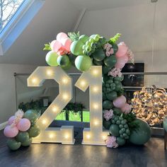 a decorated table with balloons and lights in the shape of number twenty two surrounded by greenery