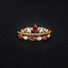 two gold rings with red and white stones on black surface next to each other,