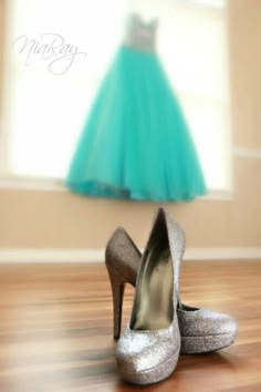 a pair of silver high heels sitting on top of a wooden floor next to a dress