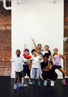 a group of people standing next to each other in front of a brick wall with their hands up