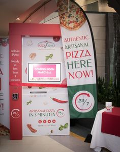 a pizza vending machine sitting next to a table with a red and white table cloth on it