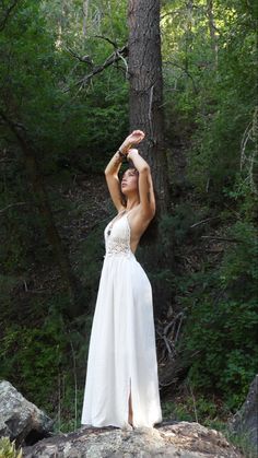 a woman in a white dress standing next to a tree with her hands on her head