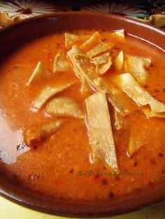 a bowl filled with soup and chips on top of a wooden table next to a spoon