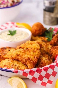 a plate with some fried food on it next to lemon wedges and dipping sauce