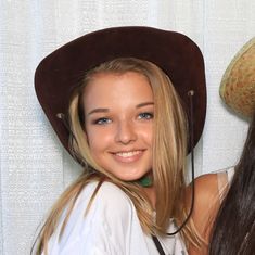 two beautiful young women standing next to each other in front of a white wall wearing hats