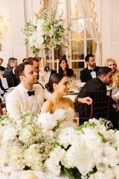 a bride and groom sitting at a table with white flowers in front of their faces