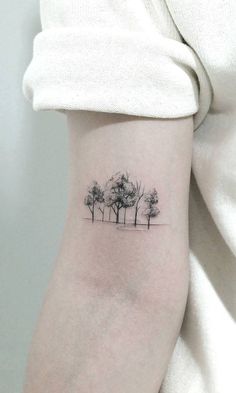 a small tree tattoo on the left inner arm, with three trees in the background