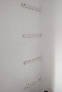 the corner of a white room with three shelves on each wall and a wood floor