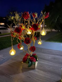 a vase filled with red roses sitting on top of a wooden table next to a tree