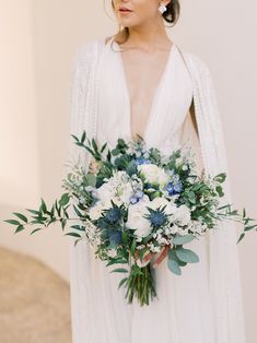 a woman wearing a white dress holding a bouquet of flowers and greenery in her hand