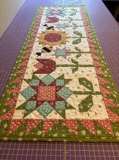 a quilted table runner made with green and pink fabrics on top of a purple cutting mat