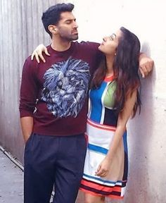 a man and woman standing next to each other near a wall with their arms around each other