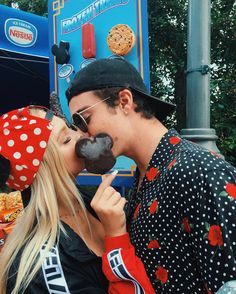 a man and woman kissing while eating chocolate covered doughnuts at an amusement park