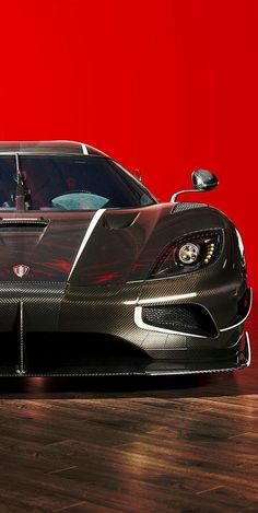 a black sports car parked on top of a wooden floor next to a red wall