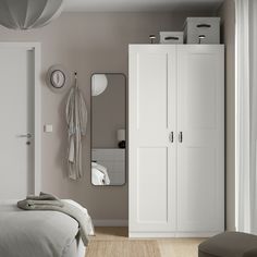 a bedroom with a bed, mirror and white cupboards in front of a window