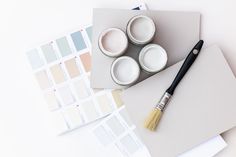 some paint cans and a brush sitting on top of a white table with color swatches