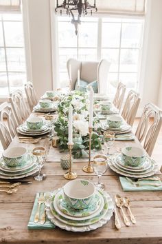 a dining room table set with plates and place settings, candlesticks and flowers