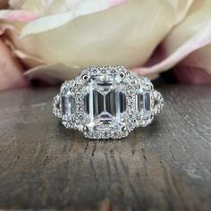 an emerald cut diamond ring on top of a wooden table with flowers in the background