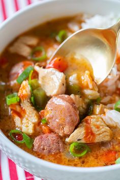 a white bowl filled with meat, rice and veggies next to a spoon