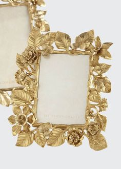 two gold frames with flowers on them sitting on a marble counter top next to each other