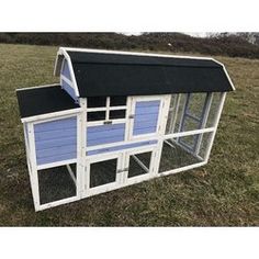 a blue and white chicken coop in the middle of a grassy field with a black roof