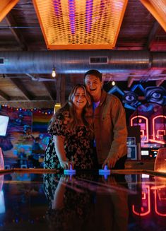 a man and woman standing next to each other in front of a bowling alley with neon lights