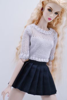 a doll with long blonde hair wearing a white sweater and black pleated skirt is posed in front of a white background