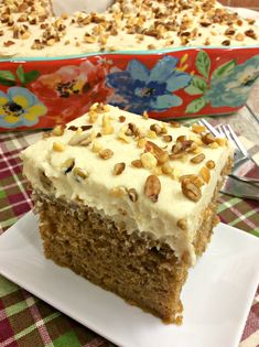 a slice of carrot cake with white frosting on a plate next to the rest of the cake