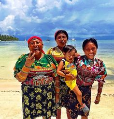 three women and a child standing on the beach with boats in the water behind them