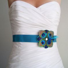 a woman wearing a white dress with a blue ribbon around the waist and peacock brooch