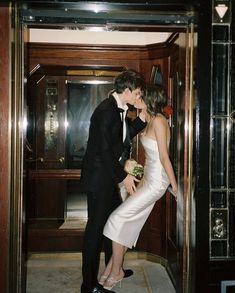 a man and woman kissing in front of an open door at the entrance to a building