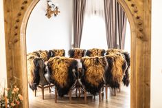 a dining room table with chairs covered in furs and an arched doorway leading to the living room