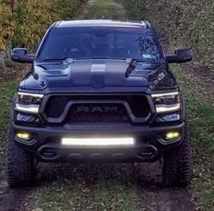 the front end of a black ram truck parked on a dirt road next to trees