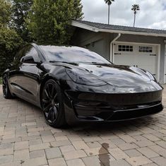 a black sports car is parked in front of a house with palm trees on the driveway