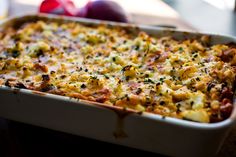 a casserole dish with cheese and vegetables in it on a table next to fruit