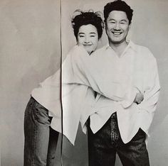 two people standing next to each other in front of a white wall with black and white photos