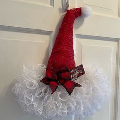 a red and white christmas wreath hanging on the front door with a santa's hat