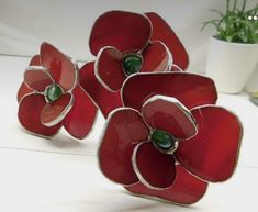 three red flower shaped vases sitting on top of a white table next to a potted plant