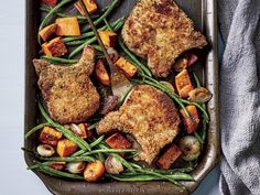 a pan filled with meat and vegetables on top of a blue table next to utensils