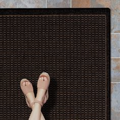 a woman's bare feet and pink sandals on a mat in front of a tiled wall