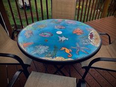 an outdoor table with fish painted on it and two chairs sitting in front of it