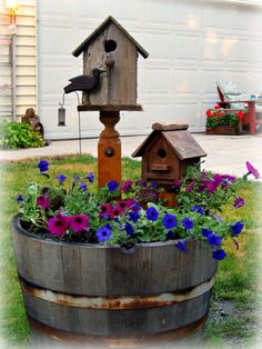 a birdhouse sitting on top of a wooden barrel filled with purple and blue flowers