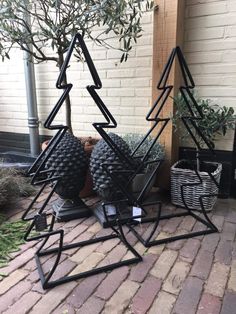 three black metal christmas trees on display in front of a brick building with potted plants