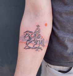 a man with a tattoo on his arm is riding a horse and has an orange dot in the background