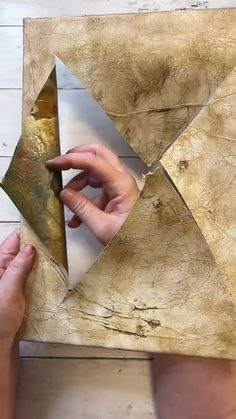 two hands are working on an origami piece with gold leaf and metal foil