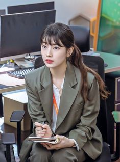 a woman sitting in front of a computer desk holding a clipboard and looking at the camera