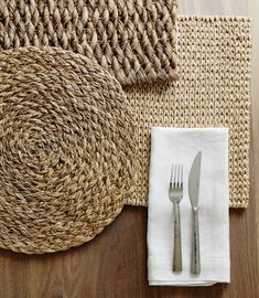 a place setting with silverware and napkins on top of woven rugs in natural colors