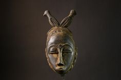 a bronze mask with two birds perched on it's head and one eye closed