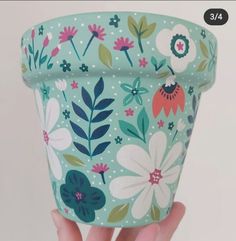 a hand holding up a flower pot with flowers on it